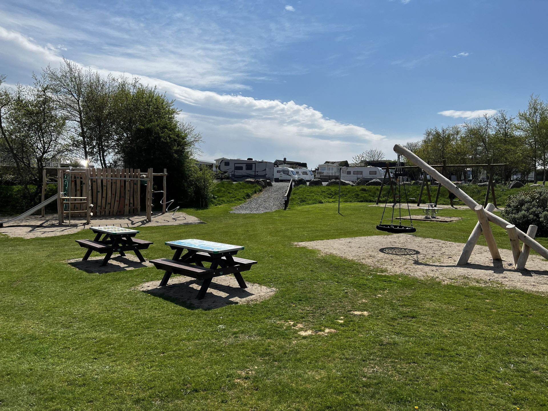 Children's play area at Pen Parc — climbing frame, swings and picnic tables in the meadow